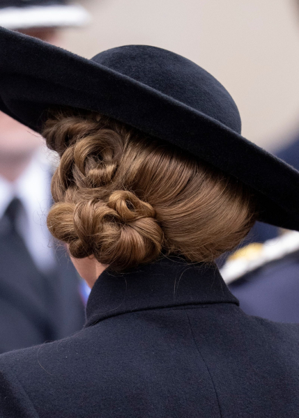 Kate Middleton wears a knotted twisted side bun under a black hat.